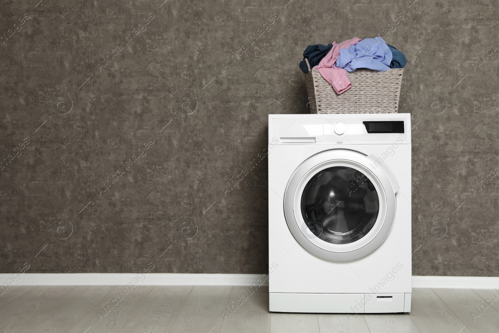 Photo of Wicker laundry basket full of dirty clothes on washing machine near color wall. Space for text