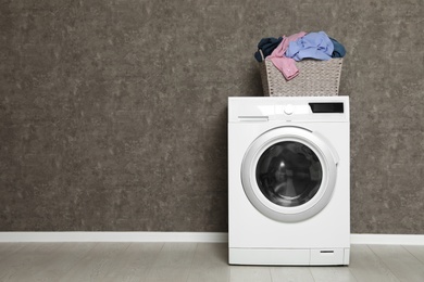 Wicker laundry basket full of dirty clothes on washing machine near color wall. Space for text