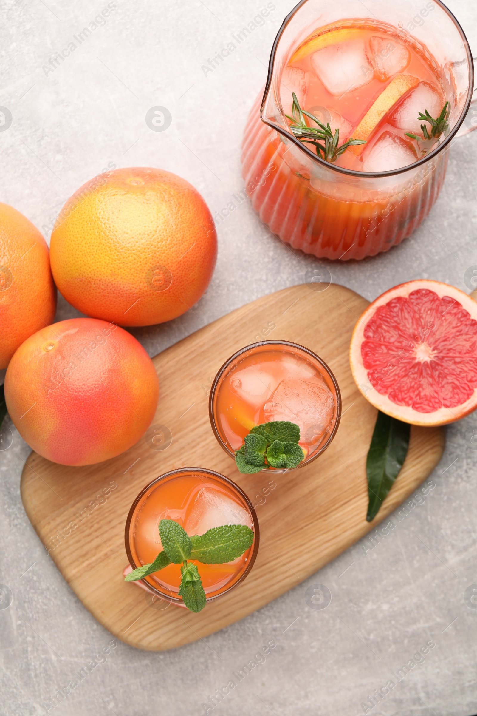 Photo of Tasty freshly made grapefruit juice, fruits and mint on light grey table, flat lay