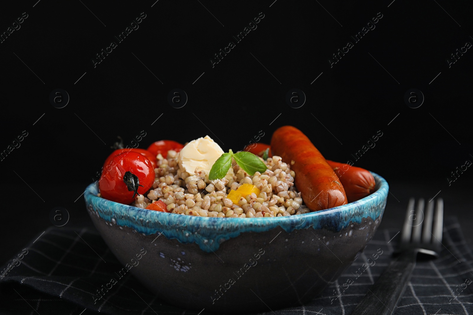 Photo of Tasty buckwheat porridge with sausages on table against black background