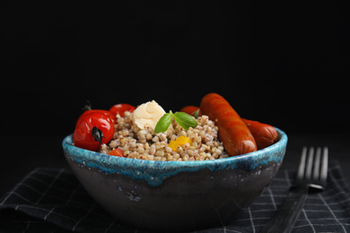 Photo of Tasty buckwheat porridge with sausages on table against black background