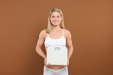 Photo of Slim woman holding scales on brown background. Weight loss