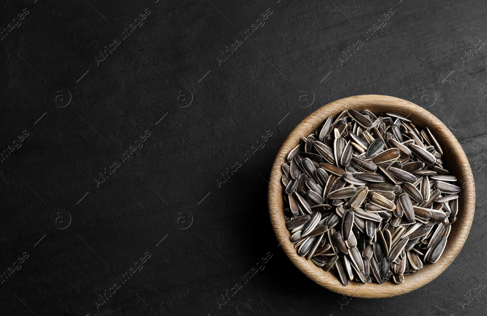 Photo of Raw sunflower seeds in bowl on black table, top view. Space for text