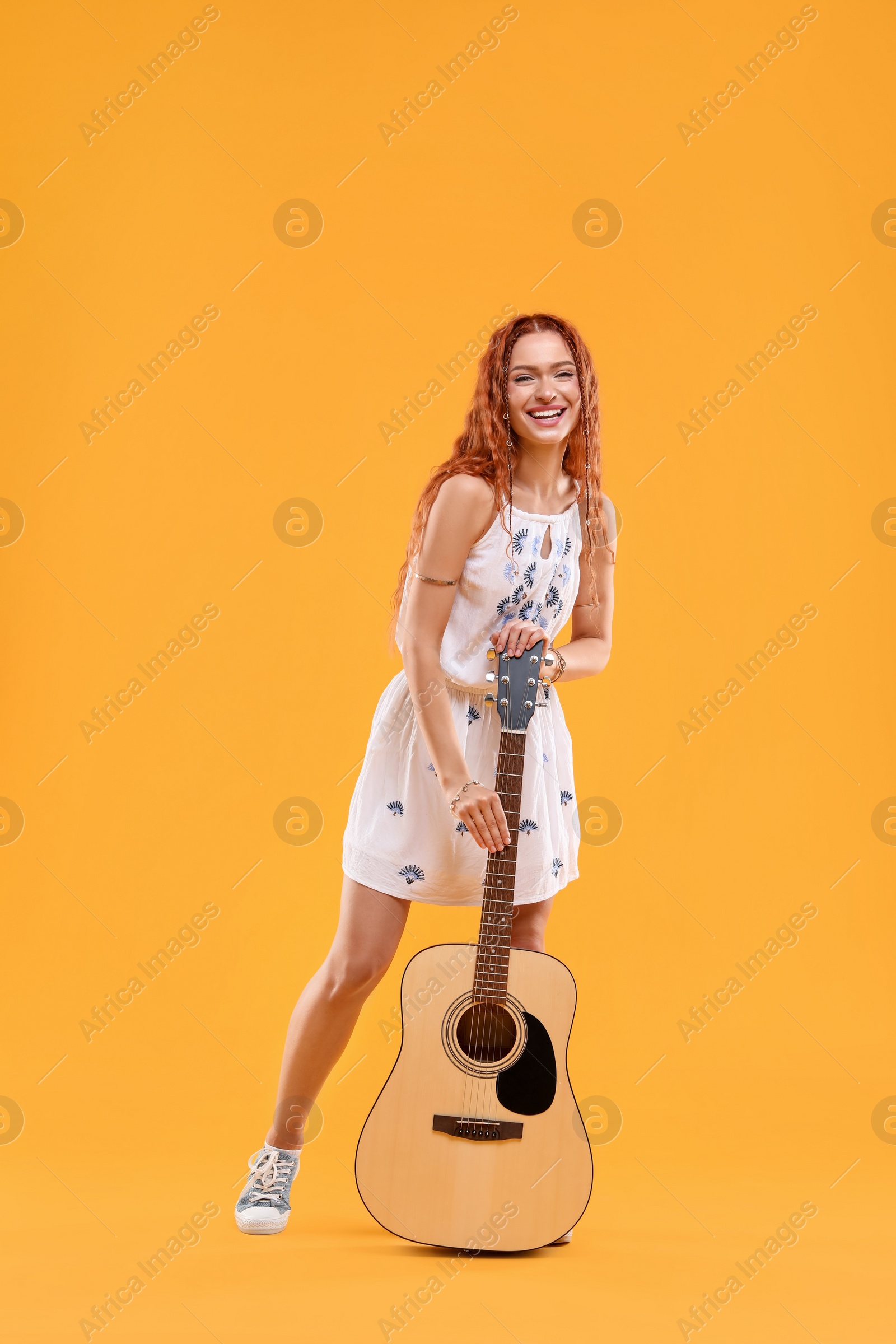 Photo of Beautiful young hippie woman with guitar on orange background