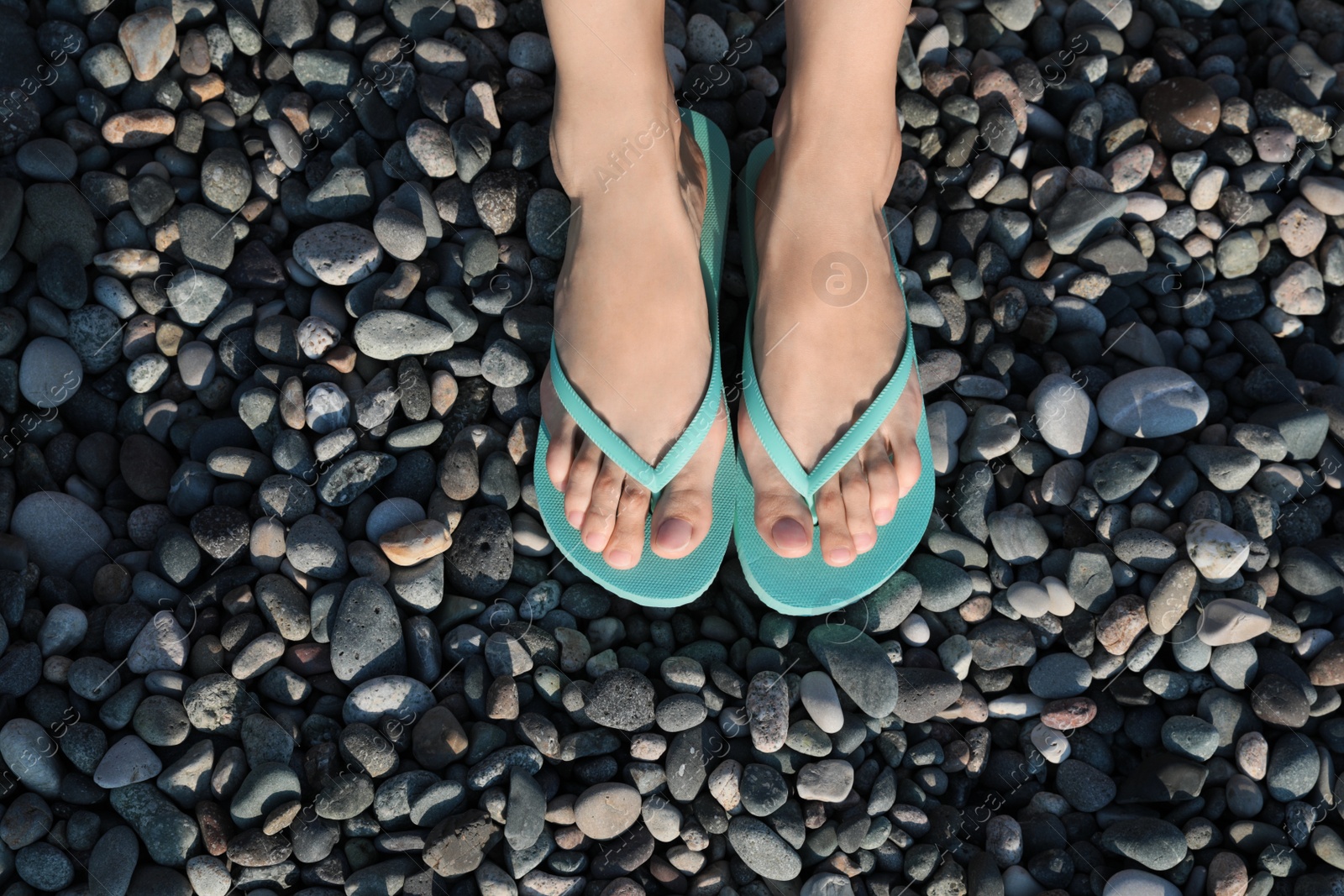 Photo of Woman in stylish flip flops on pebble beach, closeup