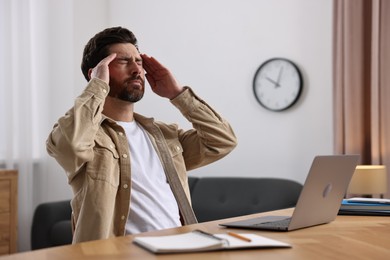 Photo of Tired man suffering from headache at workplace in office