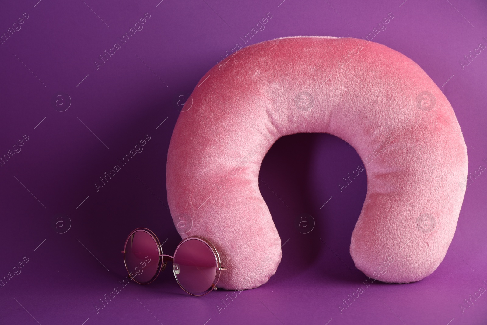 Photo of Pink travel pillow and sunglasses on violet background