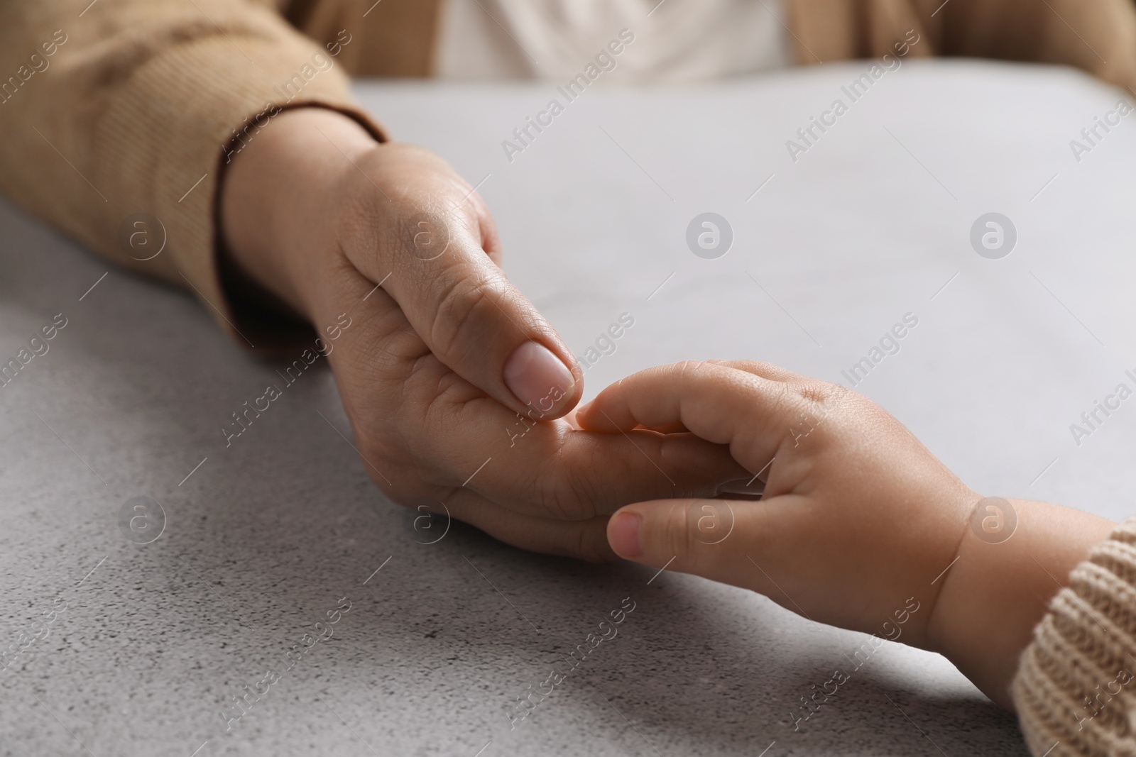 Photo of Woman holding hands with her little daughter at light grey table, closeup