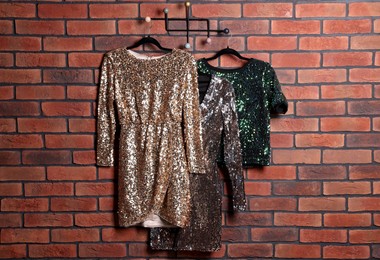 Photo of Different shiny beautiful women's party dresses on hangers near brick wall. Stylish trendy clothes for high school prom