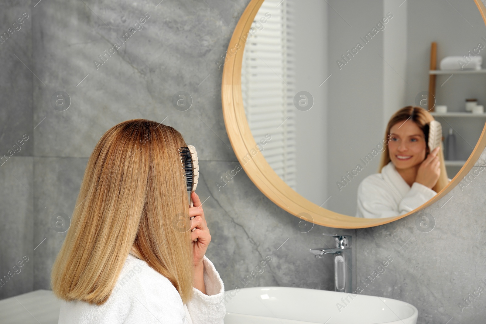 Photo of Beautiful woman brushing her hair near mirror in bathroom