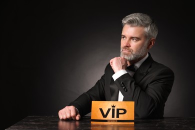 Handsome man sitting at table with VIP sign on black background. Space for text