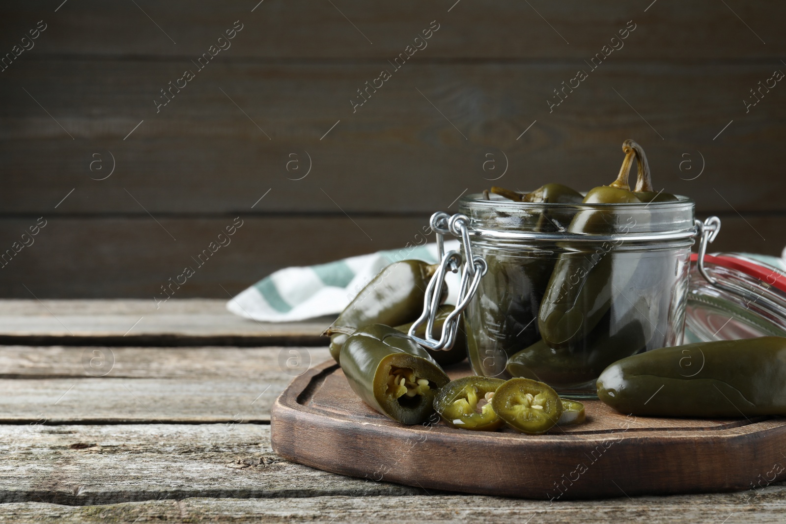 Photo of Pickled green jalapeno peppers on wooden table, space for text