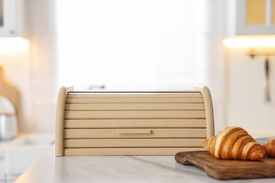Photo of Wooden bread box and board with croissants on white marble table in kitchen