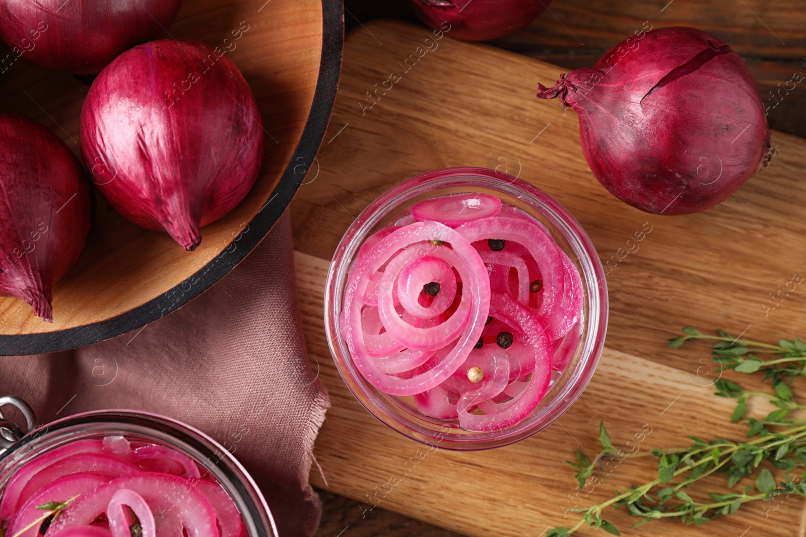 Photo of Composition with tasty pickled onions on wooden cutting board, flat lay