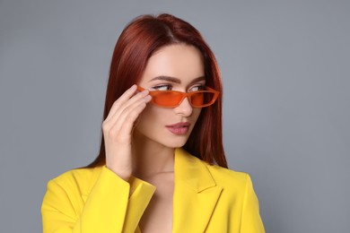 Photo of Stylish woman with red dyed hair and orange sunglasses on light gray background