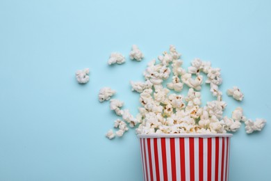 Photo of Overturned paper cup with delicious popcorn on light blue background, flat lay. Space for text