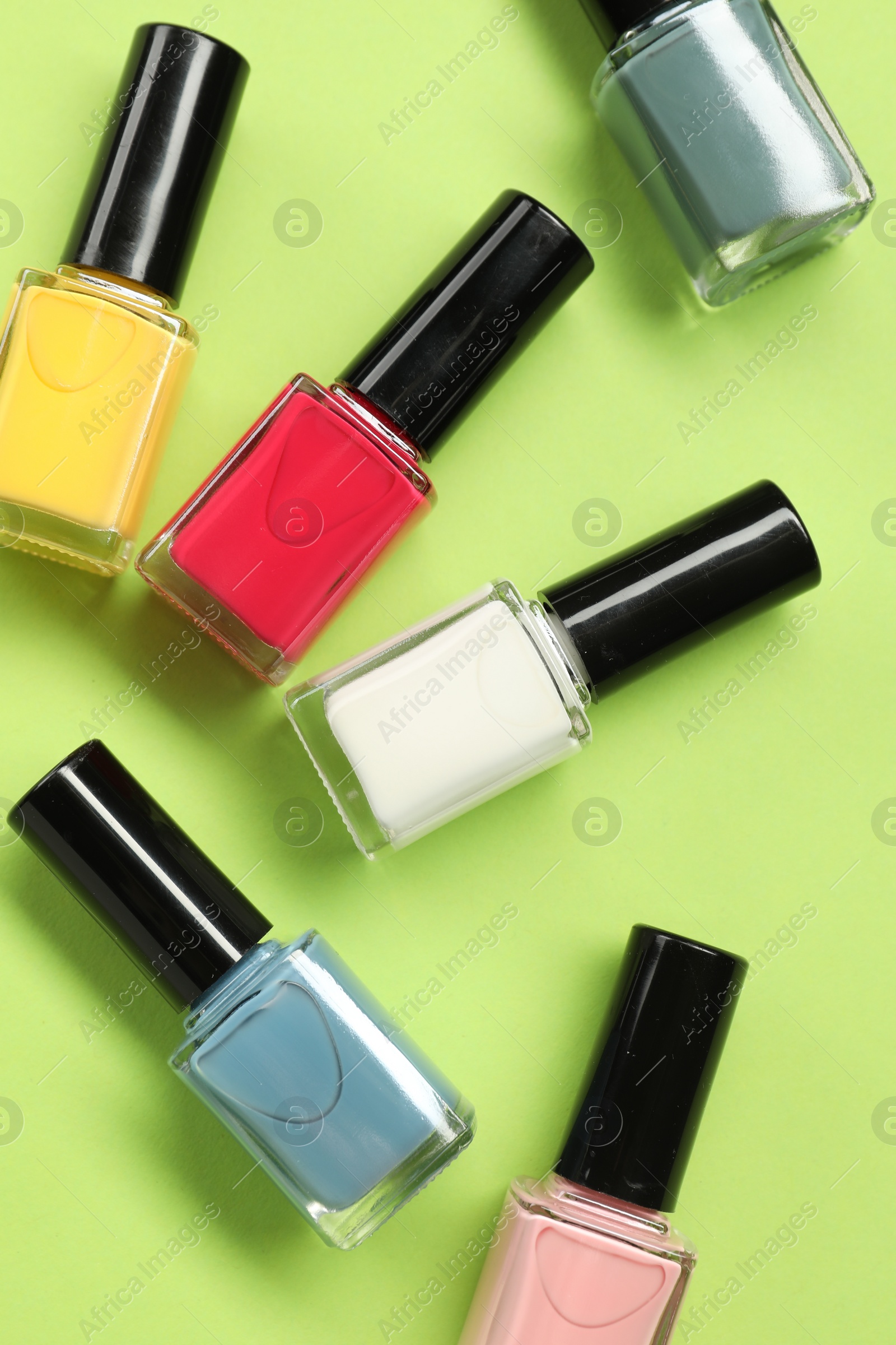 Photo of Colorful nail polishes in bottles on green background, flat lay