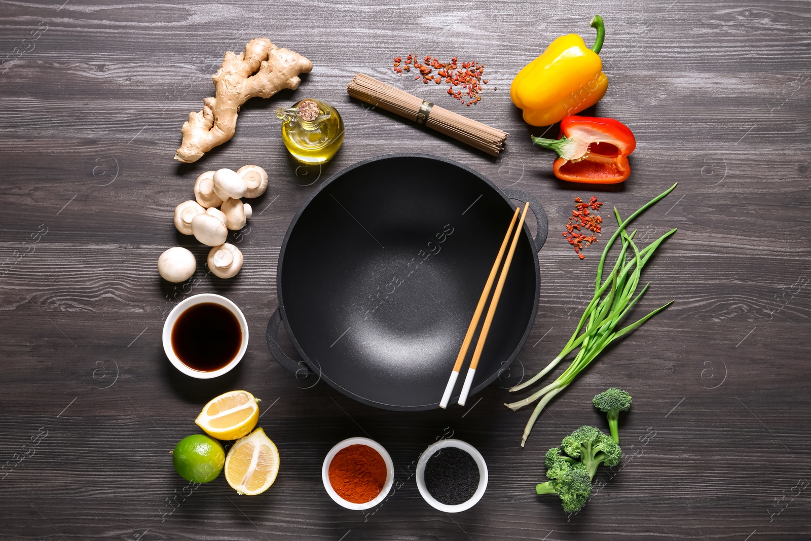 Photo of Empty iron wok and chopsticks surrounded by ingredients on dark grey wooden table, flat lay