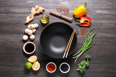 Photo of Empty iron wok and chopsticks surrounded by ingredients on dark grey wooden table, flat lay