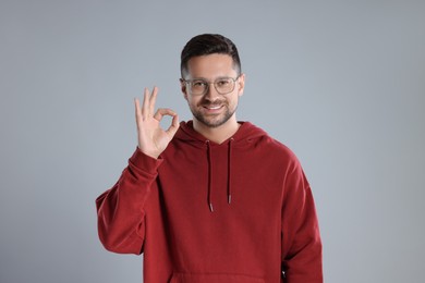 Portrait of happy man in stylish glasses showing ok gesture on light grey background