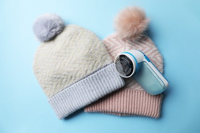 Modern fabric shaver and woolen hats on light blue background, flat lay