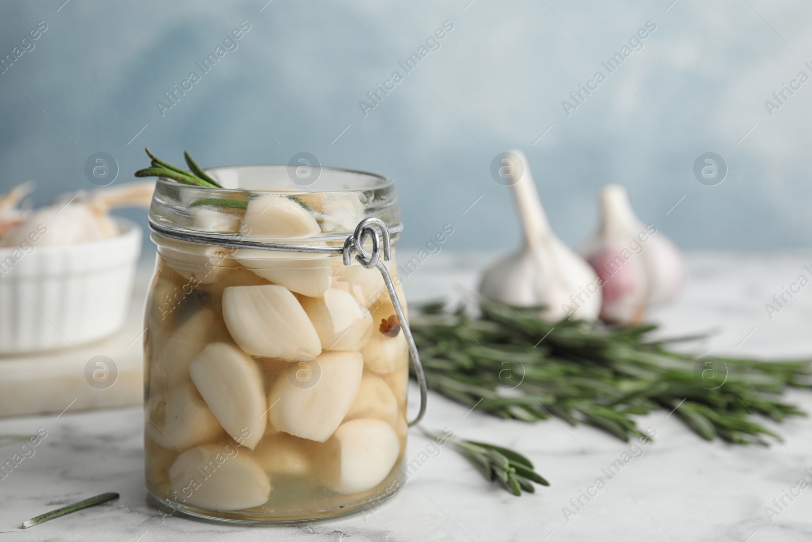 Photo of Composition with jar of pickled garlic on marble table against blue background. Space for text