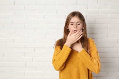 Photo of Teenage girl suffering from cough near brick wall. Space for text