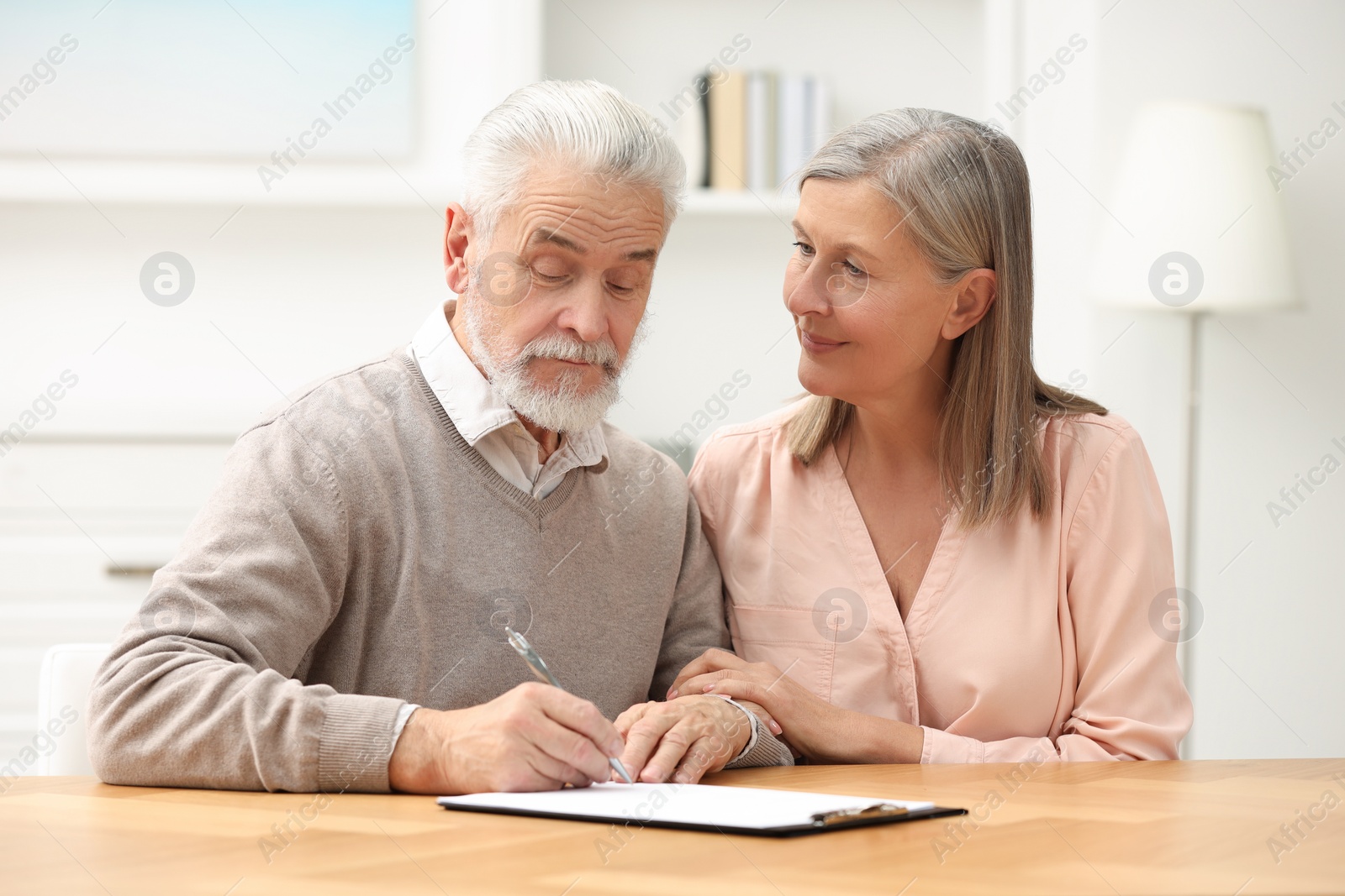 Photo of Senior couple signing Last Will and Testament indoors