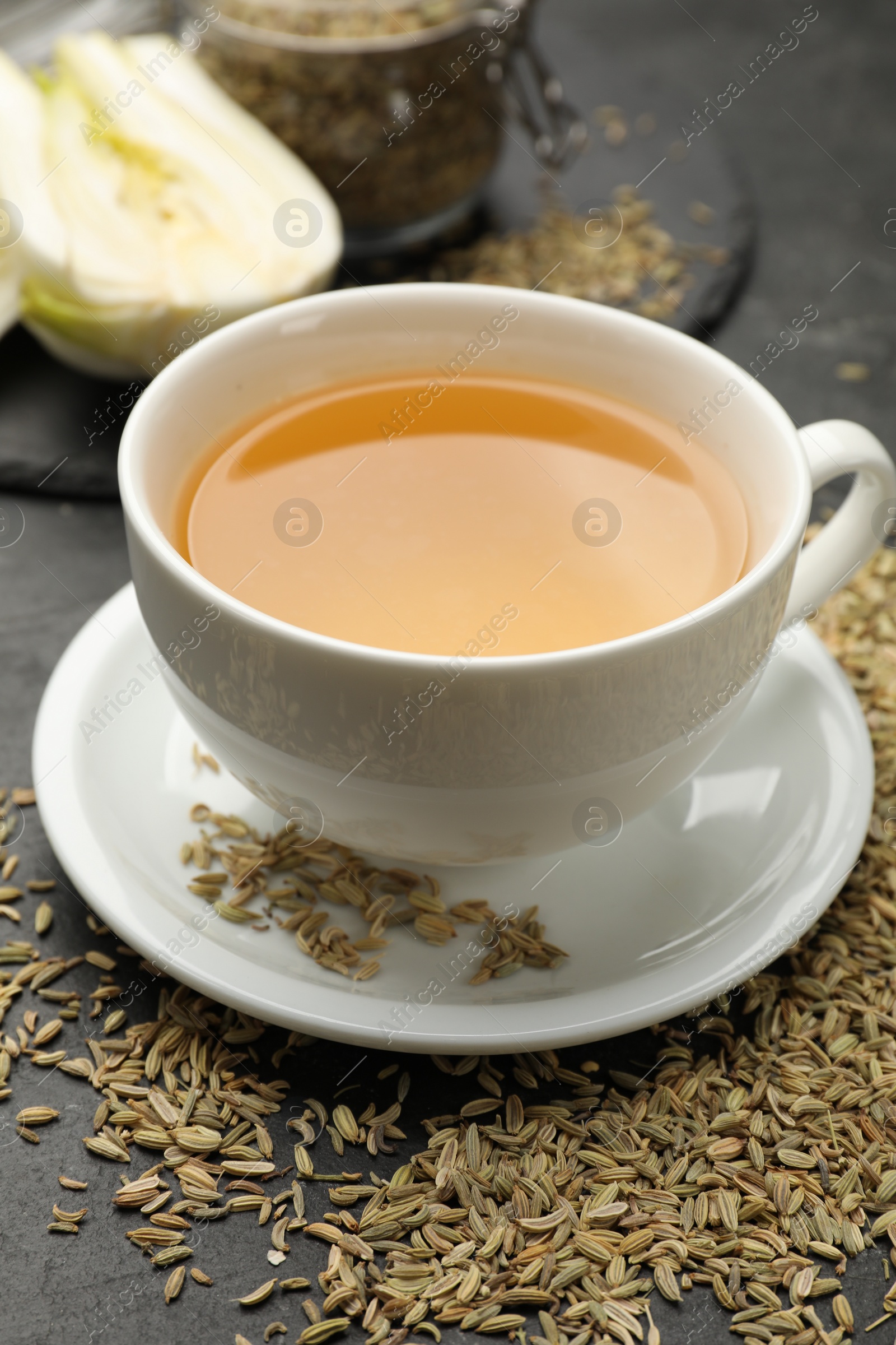 Photo of Aromatic fennel tea in cup and seeds on black table, closeup