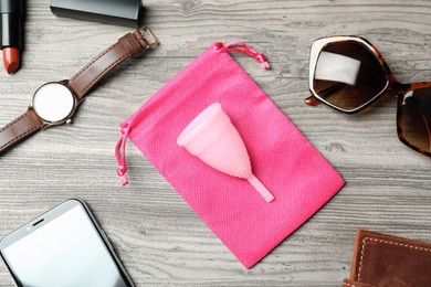 Menstrual cup and different women's accessories on wooden table, flat lay