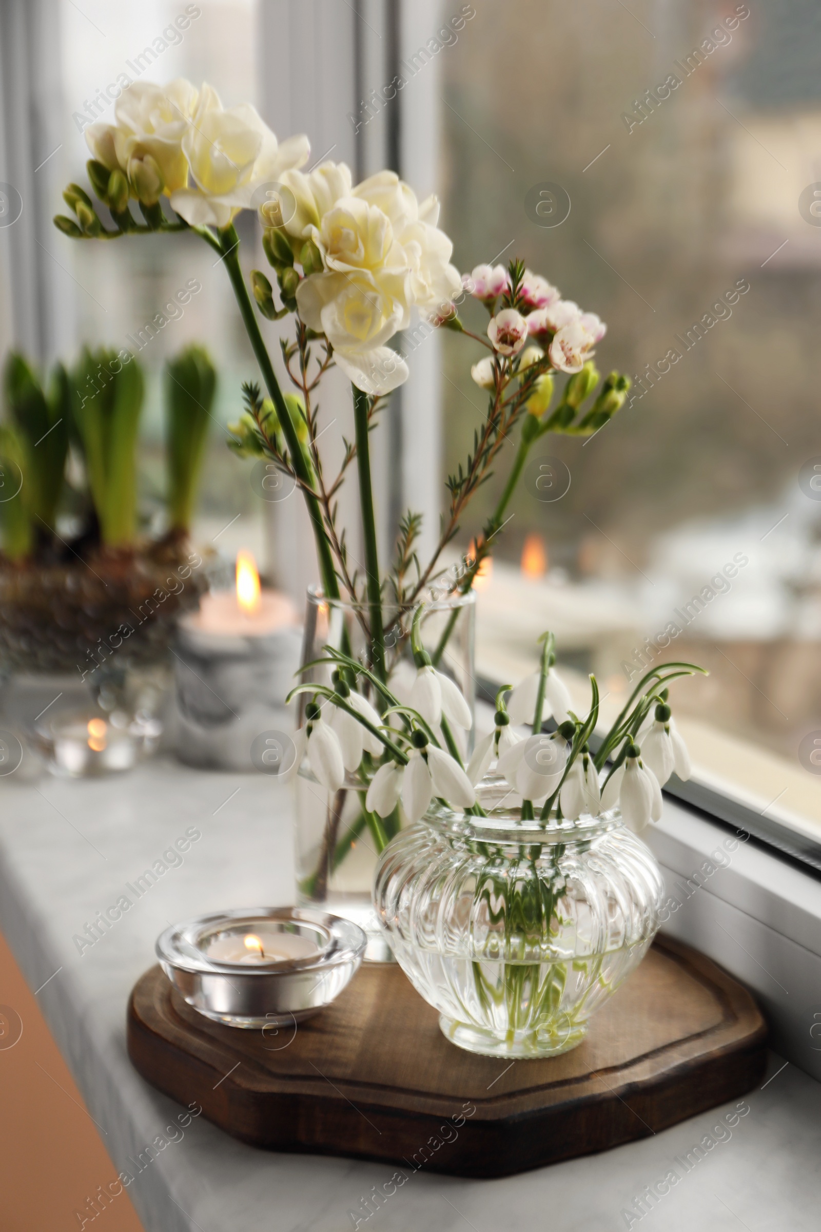 Photo of Different beautiful spring flowers and candles on windowsill indoors