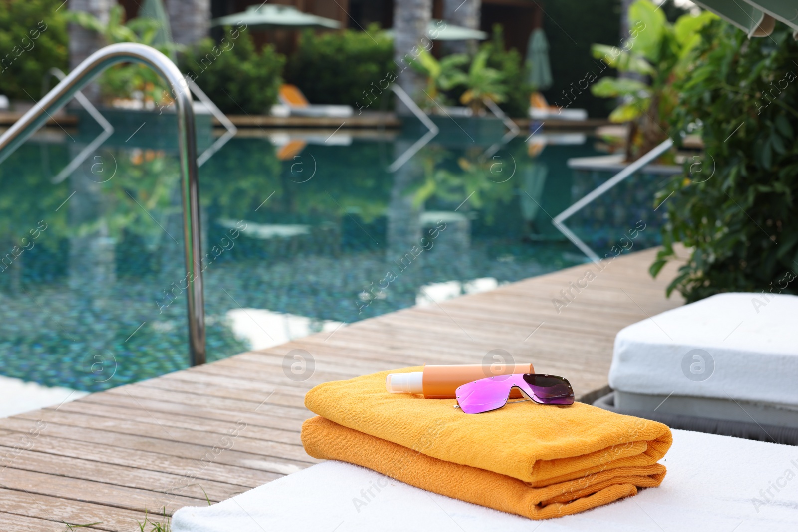 Photo of Beach towels, sunglasses and sunscreen on sun lounger near outdoor swimming pool, space for text. Luxury resort