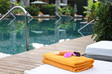 Beach towels, sunglasses and sunscreen on sun lounger near outdoor swimming pool, space for text. Luxury resort