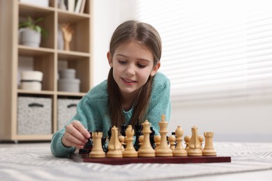 Photo of Cute girl playing chess on floor in room