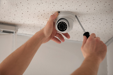 Technician installing CCTV camera on ceiling indoors, closeup