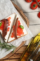 Delicious sandwiches with cream cheese, anchovies, tomatoes and basil on wooden table, flat lay