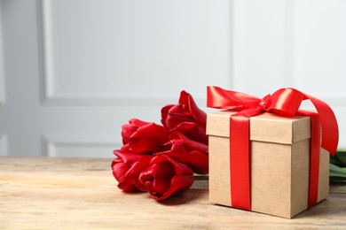 Beautiful gift box with bow and red tulips on wooden table. Space for text