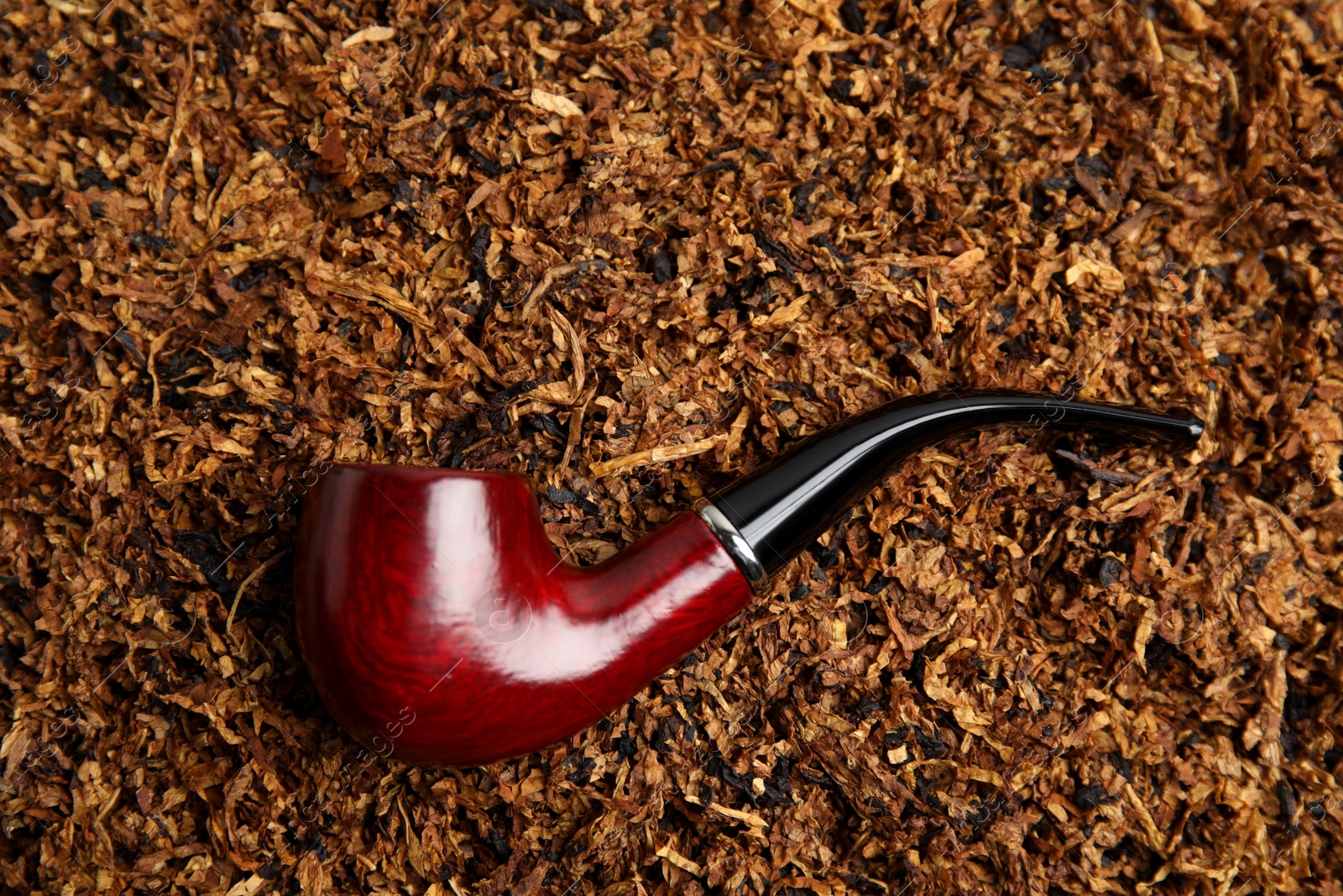 Photo of Smoking pipe on pile of tobacco, top view