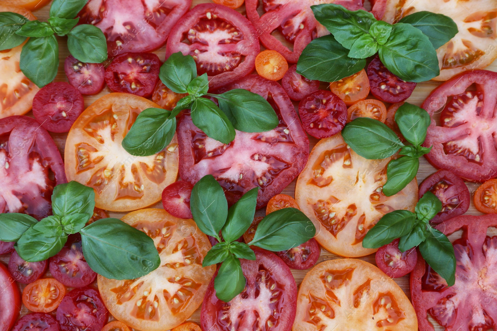 Photo of Cut tomatoes of different sorts with basil on wooden table, flat lay