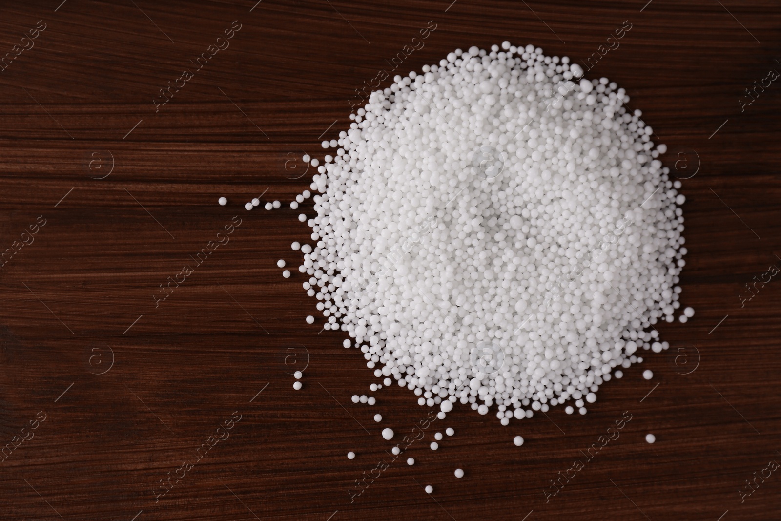 Photo of Pellets of ammonium nitrate on wooden table, flat lay with space for text. Mineral fertilizer