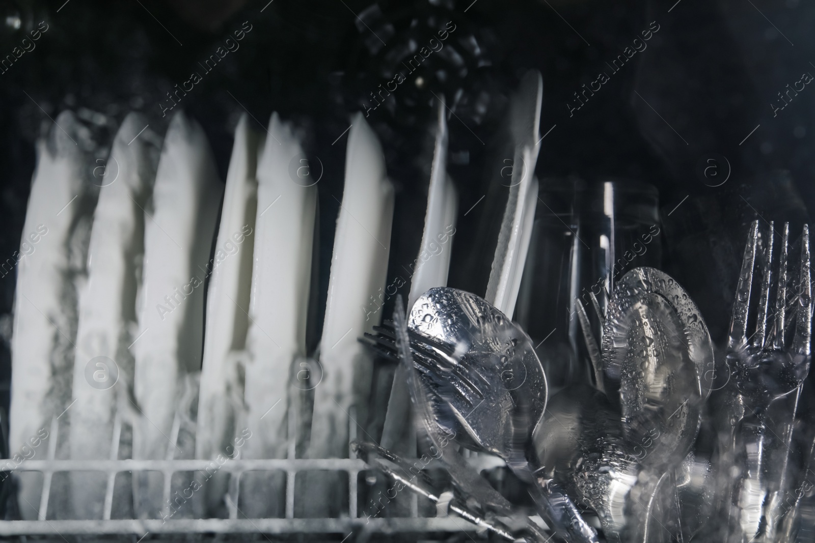 Photo of Clean plates and cutlery in dishwasher, view through wet glass