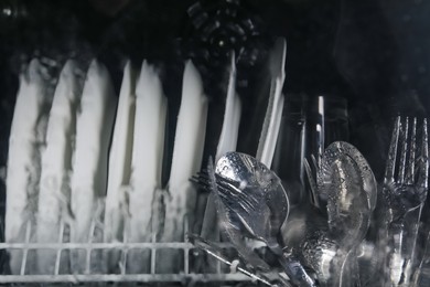 Photo of Clean plates and cutlery in dishwasher, view through wet glass