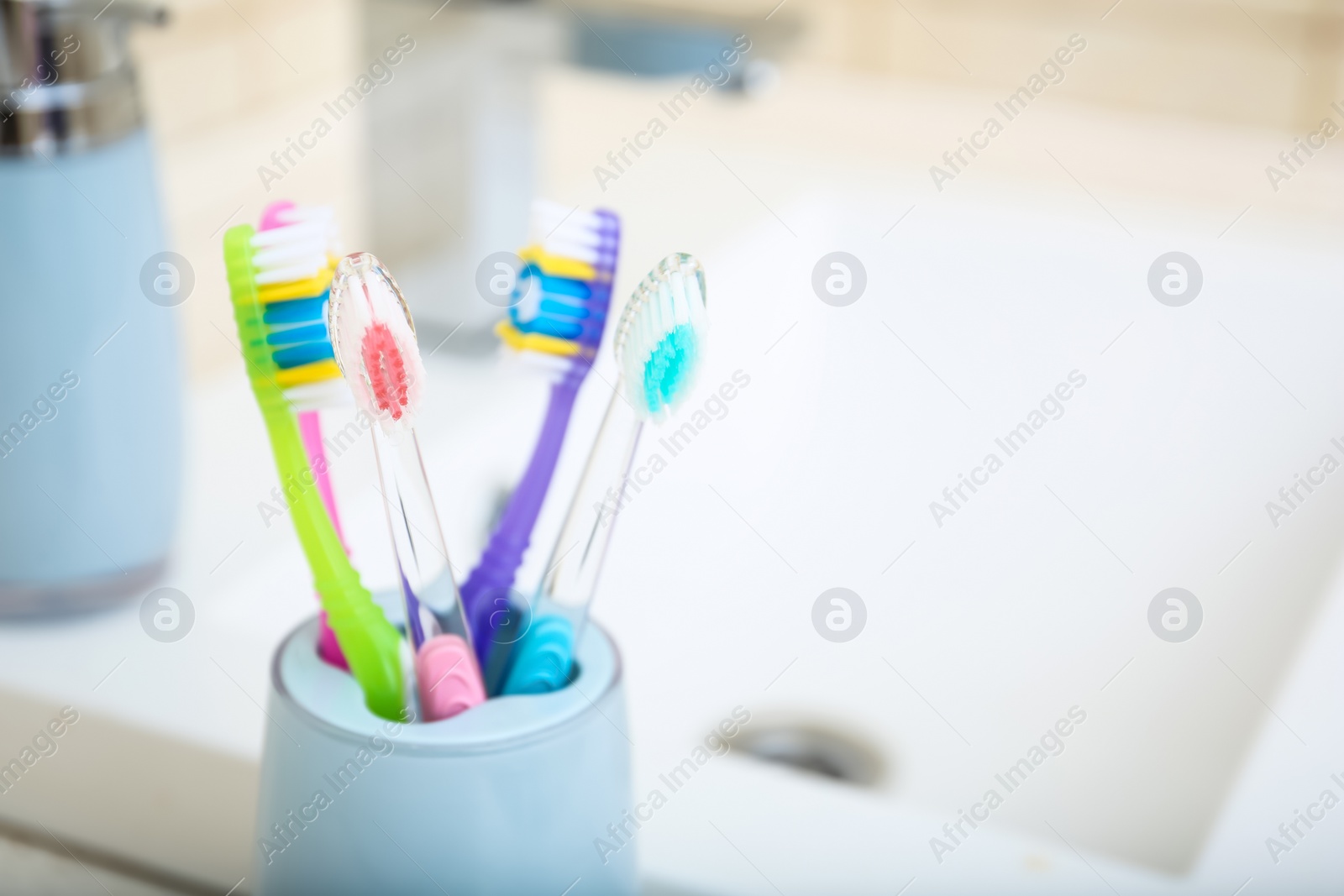 Photo of Cup with different toothbrushes near sink, closeup. Dental care