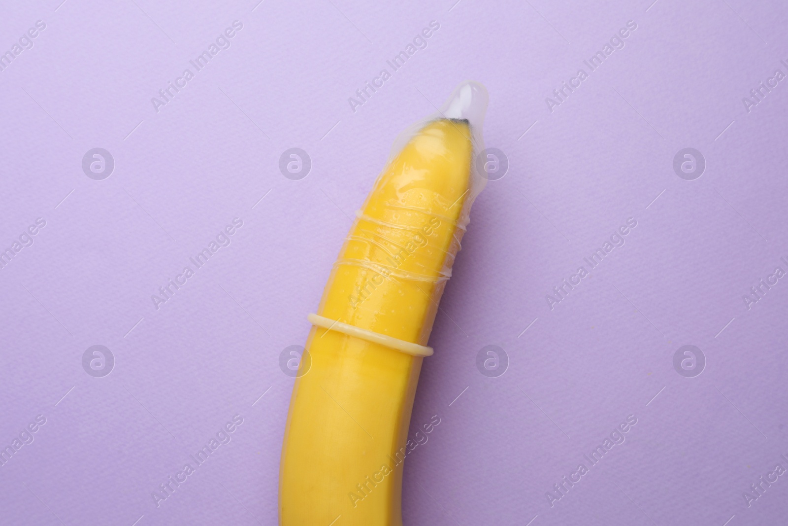 Photo of Banana with condom on lilac background, top view. Safe sex concept