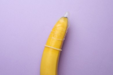 Photo of Banana with condom on lilac background, top view. Safe sex concept