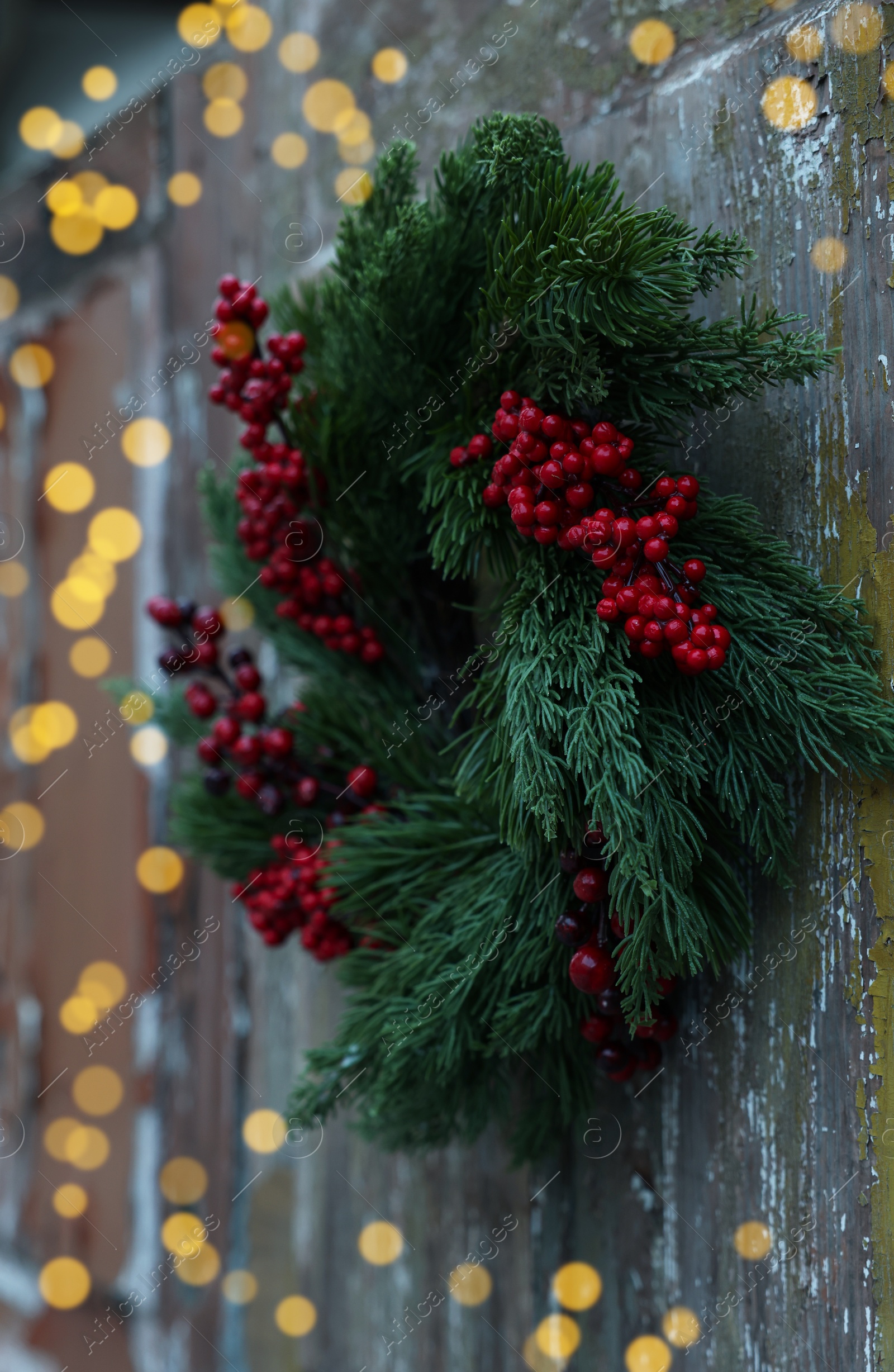 Photo of Beautiful Christmas wreath with red berries hanging on wooden wall outdoors