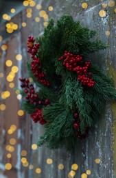 Photo of Beautiful Christmas wreath with red berries hanging on wooden wall outdoors