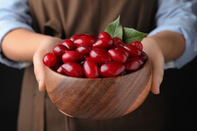 Photo of Woman with wooden bowl of fresh ripe dogwood berries on black background, closeup
