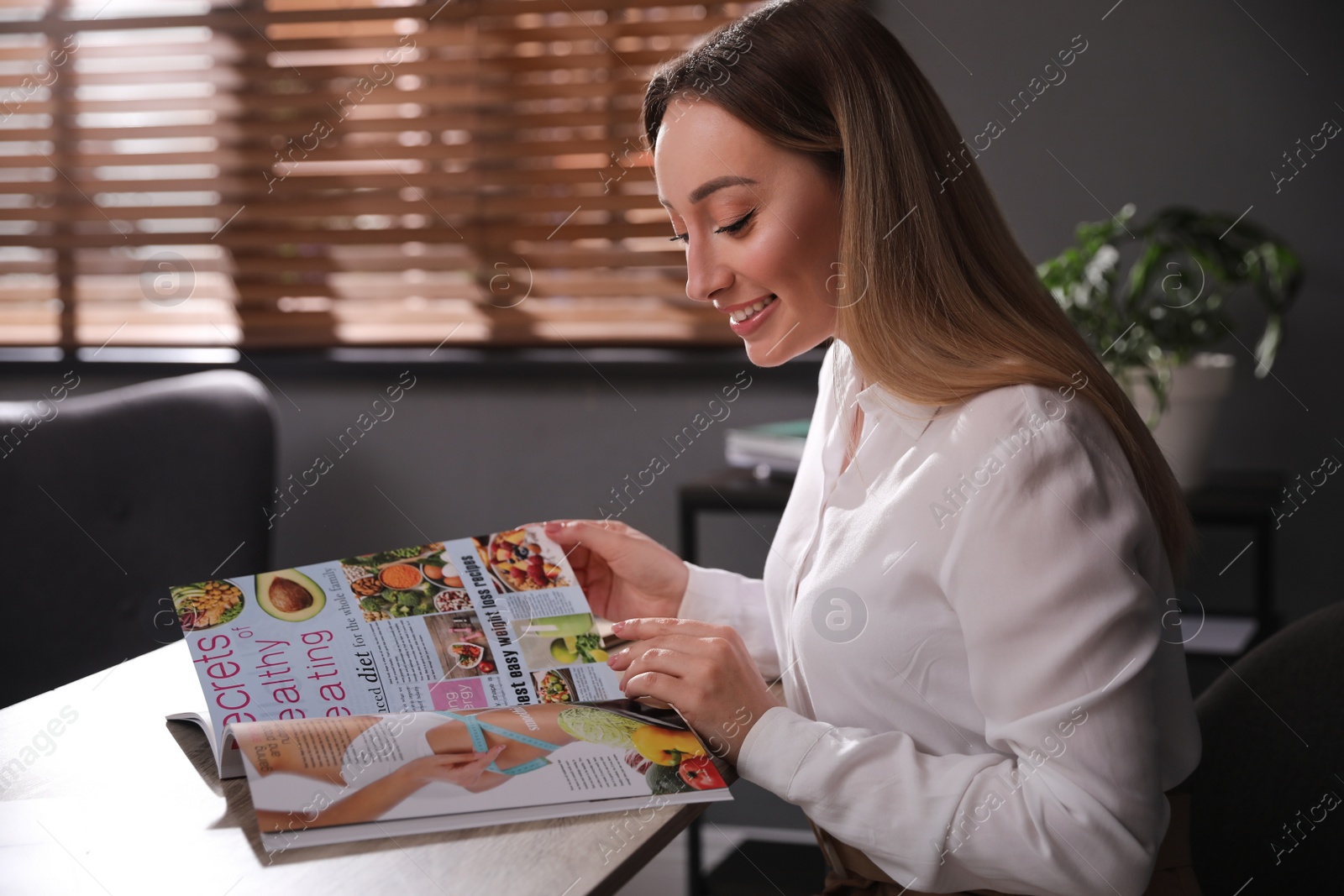 Photo of Happy woman reading magazine at workplace in office