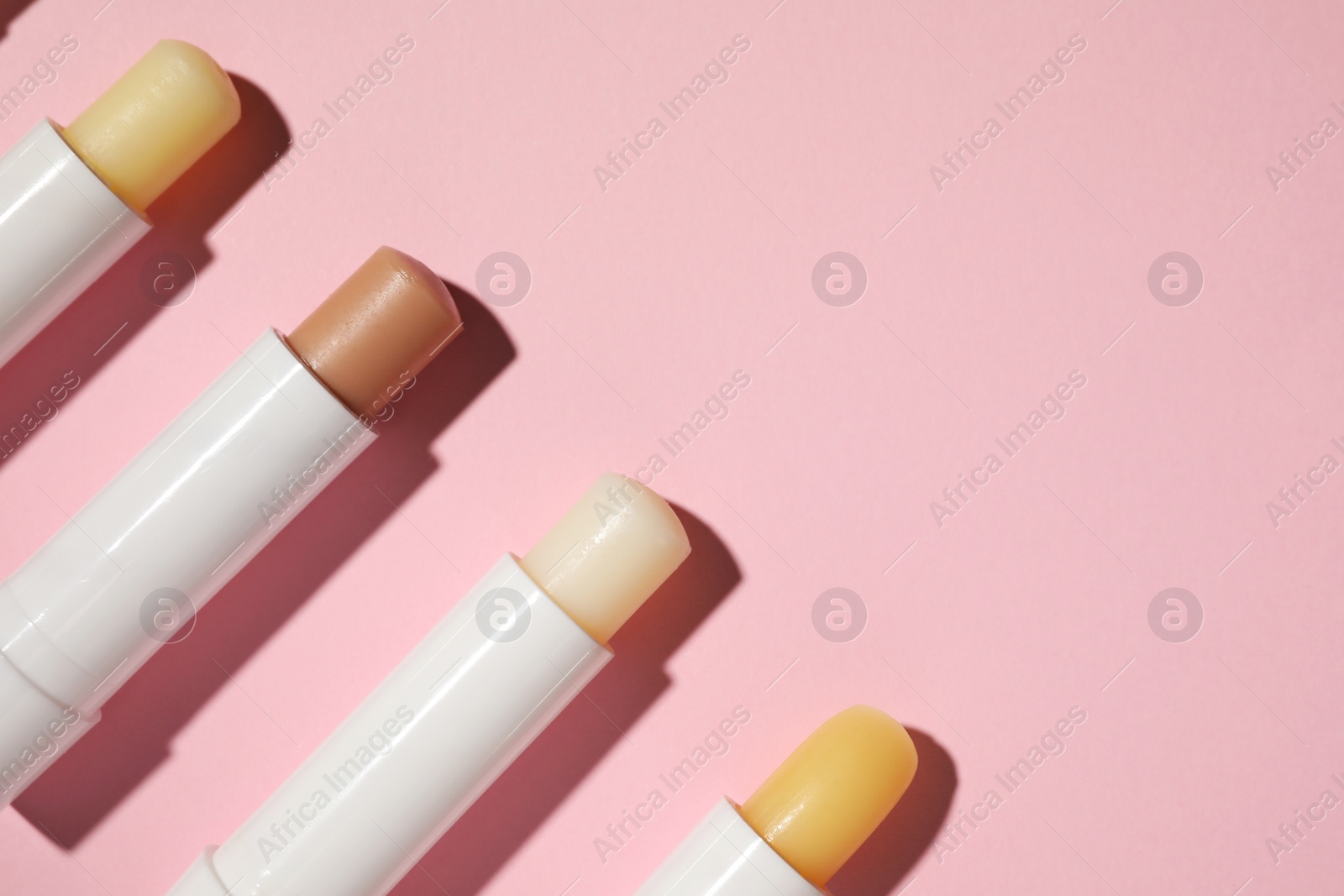 Photo of Hygienic lipsticks on pink background, flat lay. Space for text